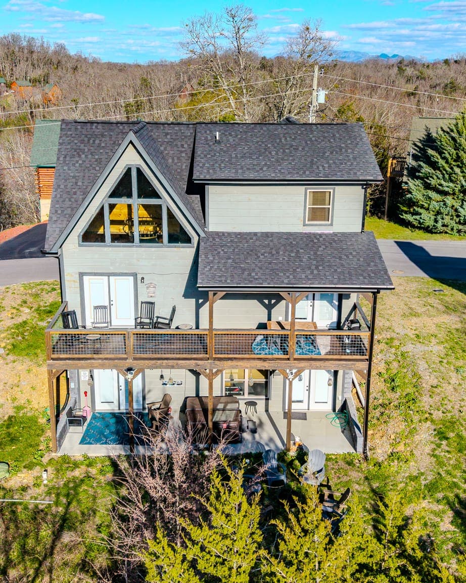 The lodge from above — prow-front gable, stacked covered decks, and the hot tub patio at the tree line